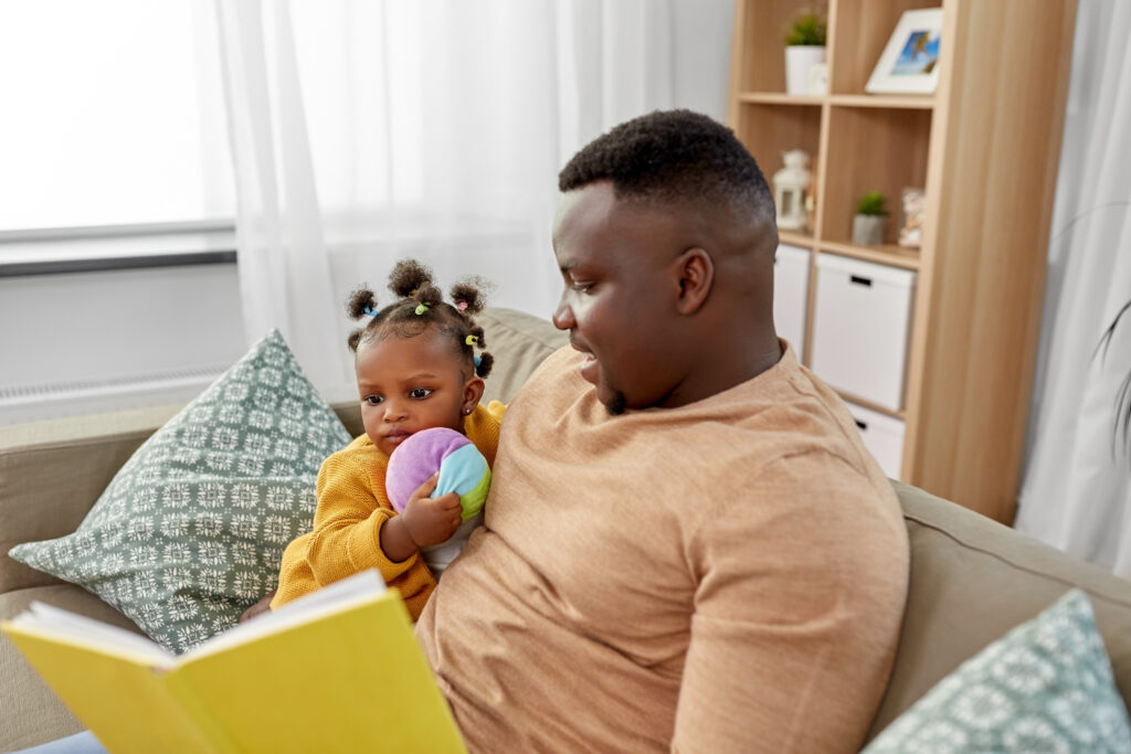 Black father reading a book to his Black infant daughter